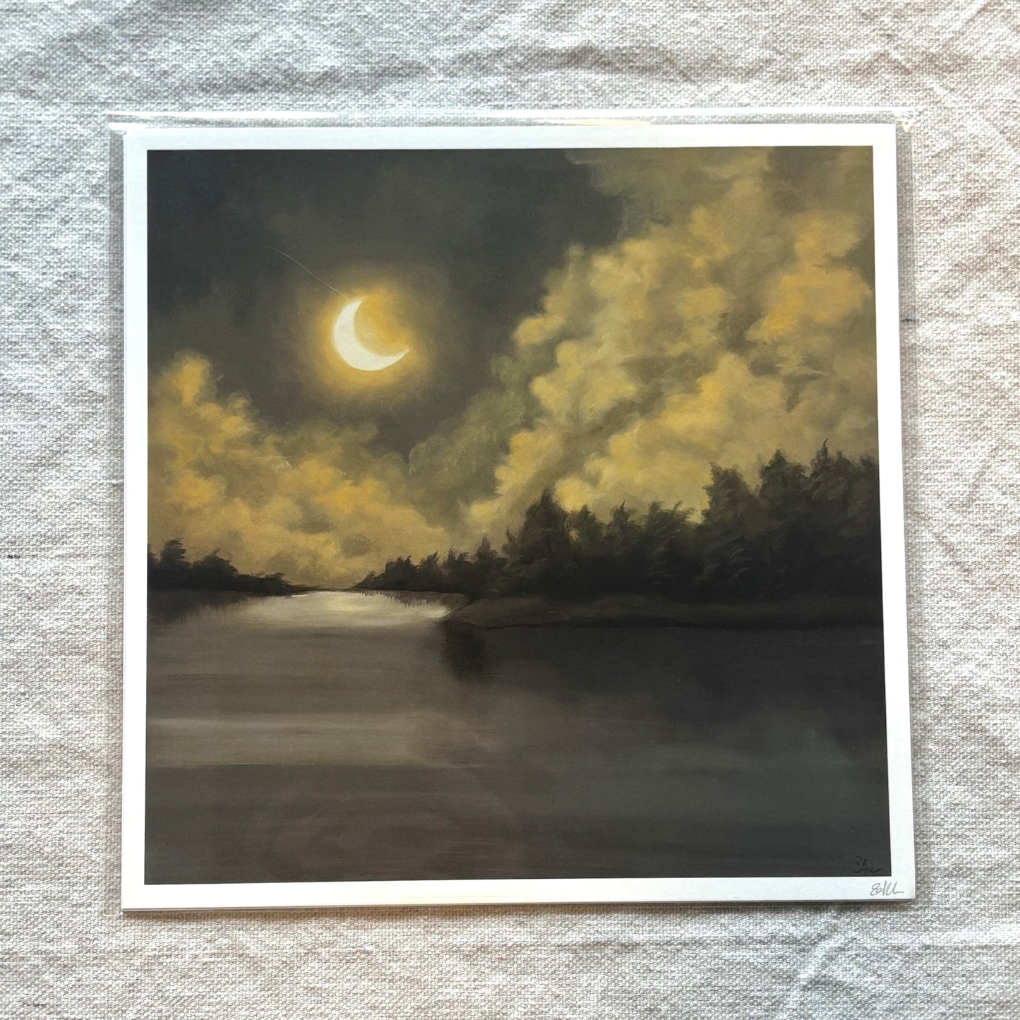 Print of a crescent moon over a forested lake on textured fabric.