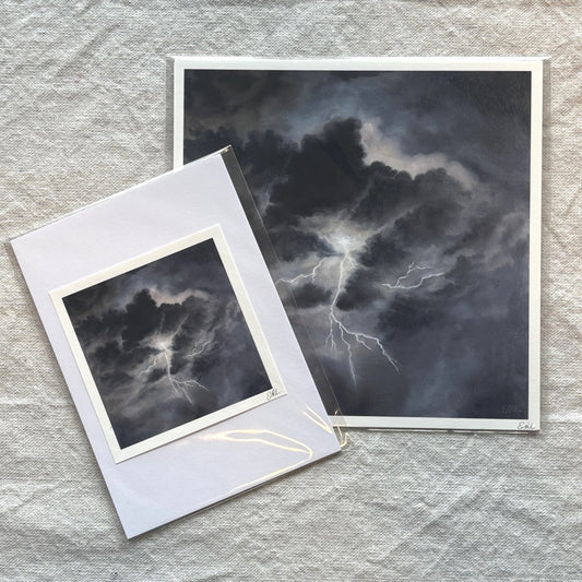Two art prints of dark cloudscapes with lightning on a textured gray surface.