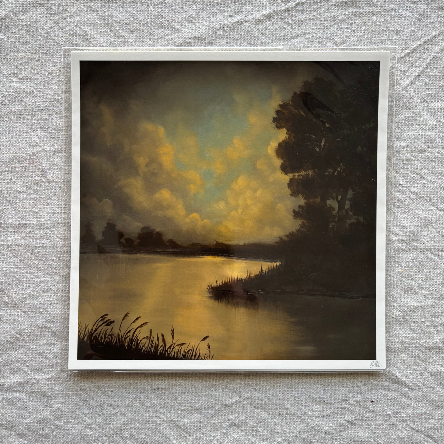 Art print of a landscape with a lake and trees on a textured gray wall.