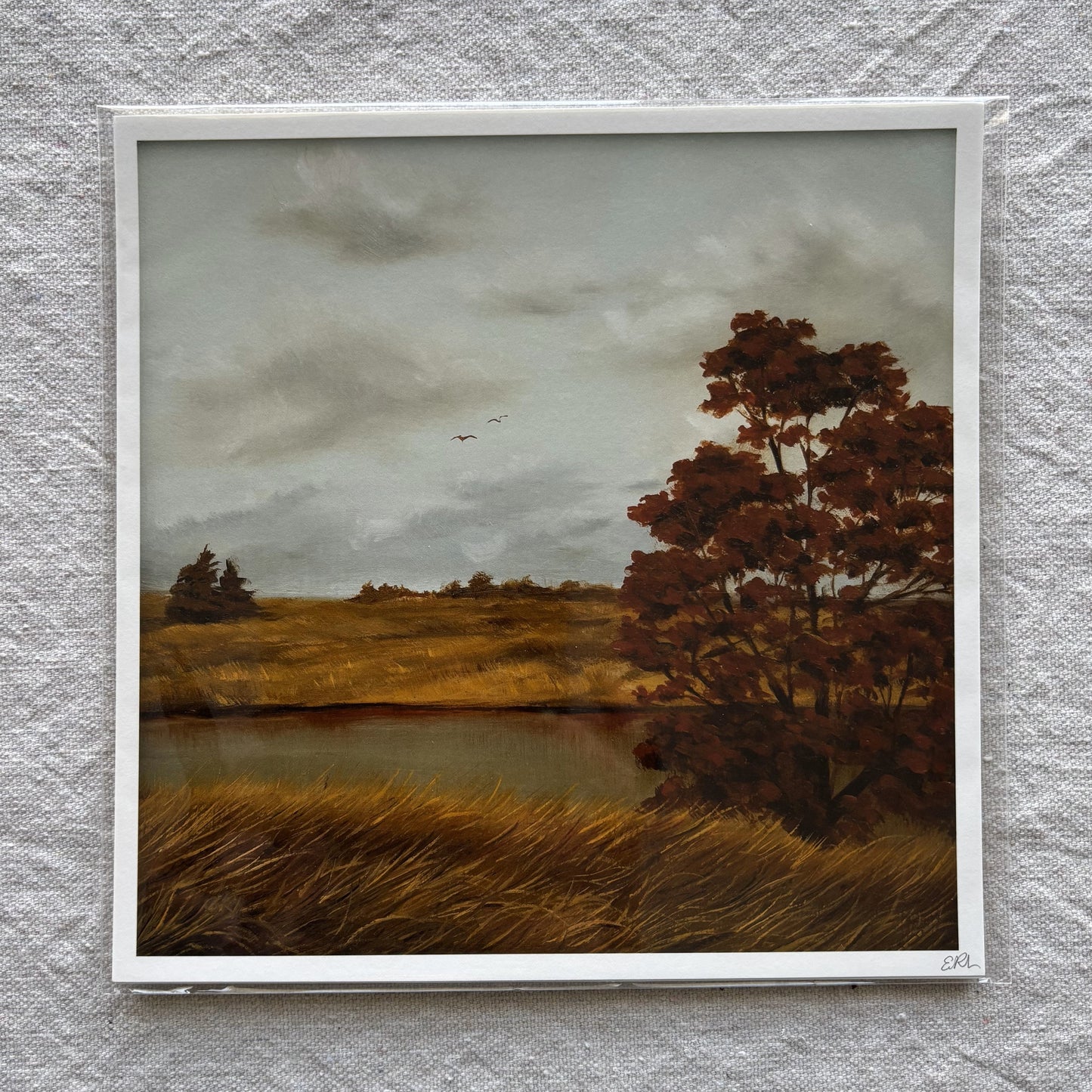 landscape art print of a field with trees and water on a textured gray wall.