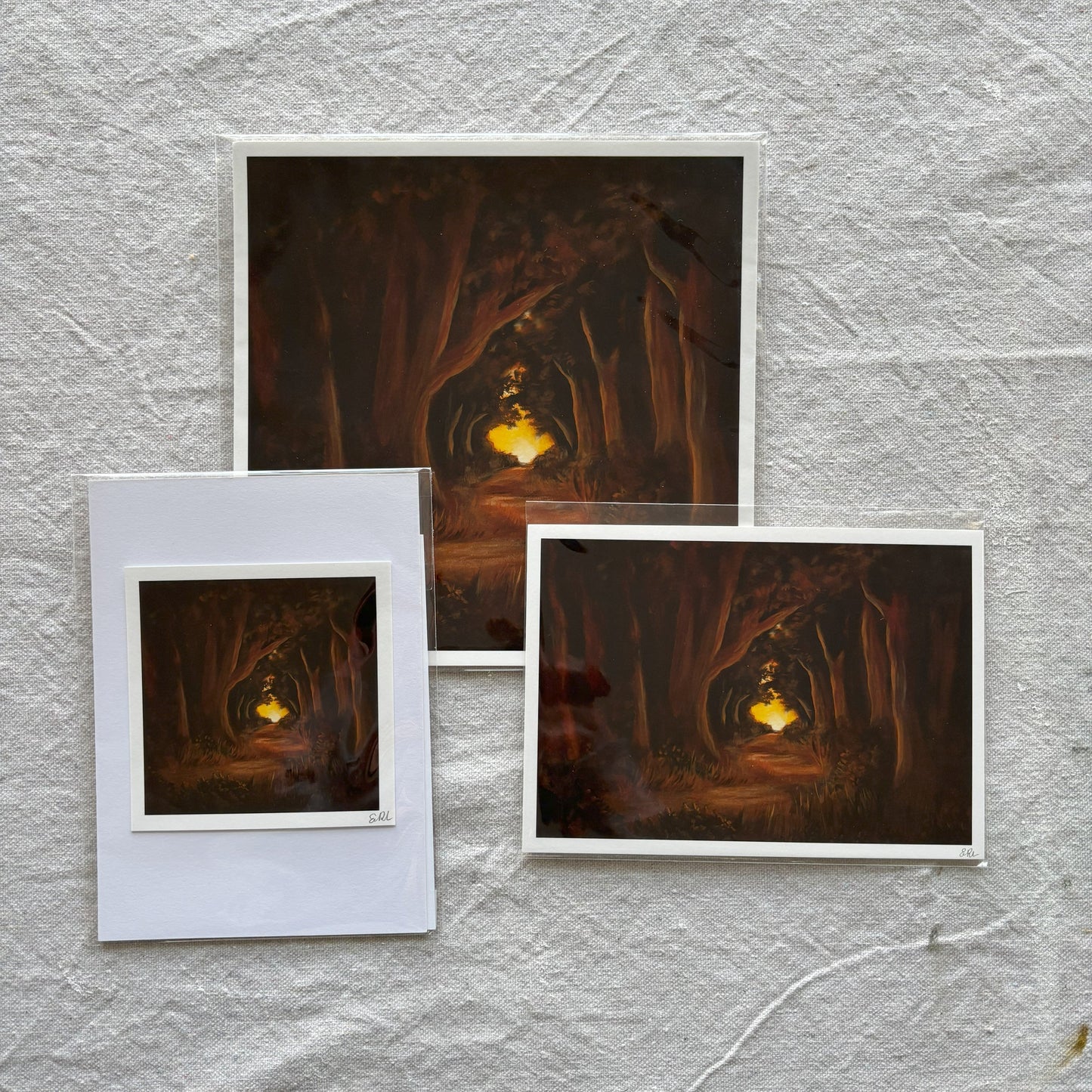 Three art print of a forest scene with a glowing light on a textured gray surface.