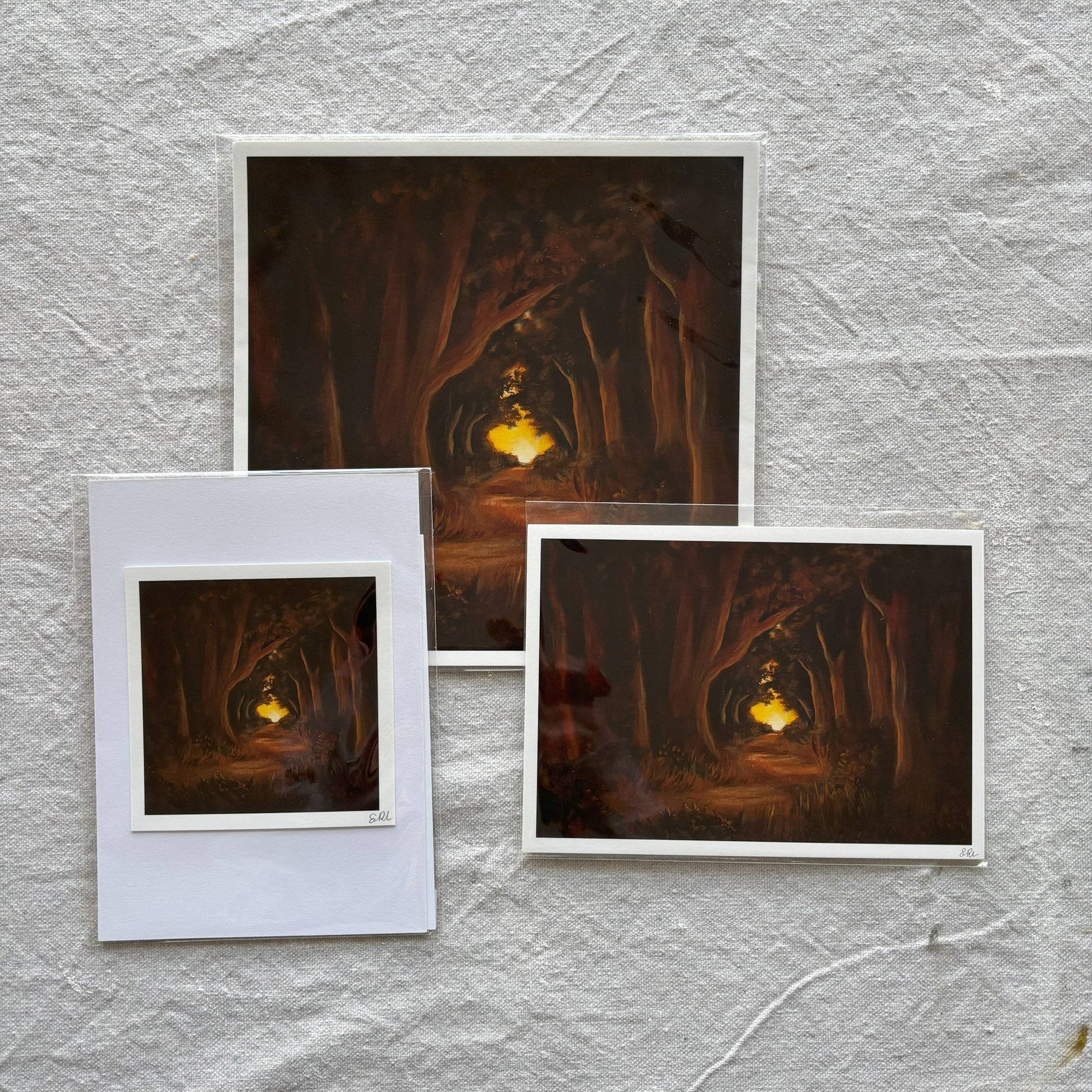 Three art print of a forest scene with a glowing light on a textured gray surface.
