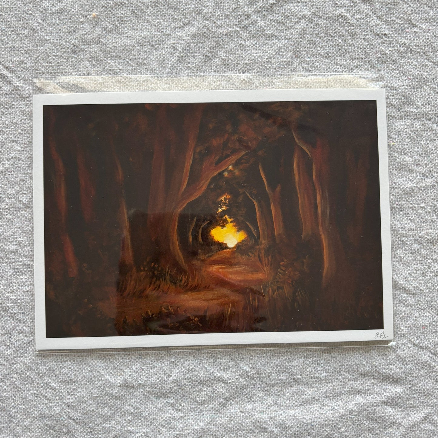 Art print of a forest scene with a glowing light at the end on textured gray paper.