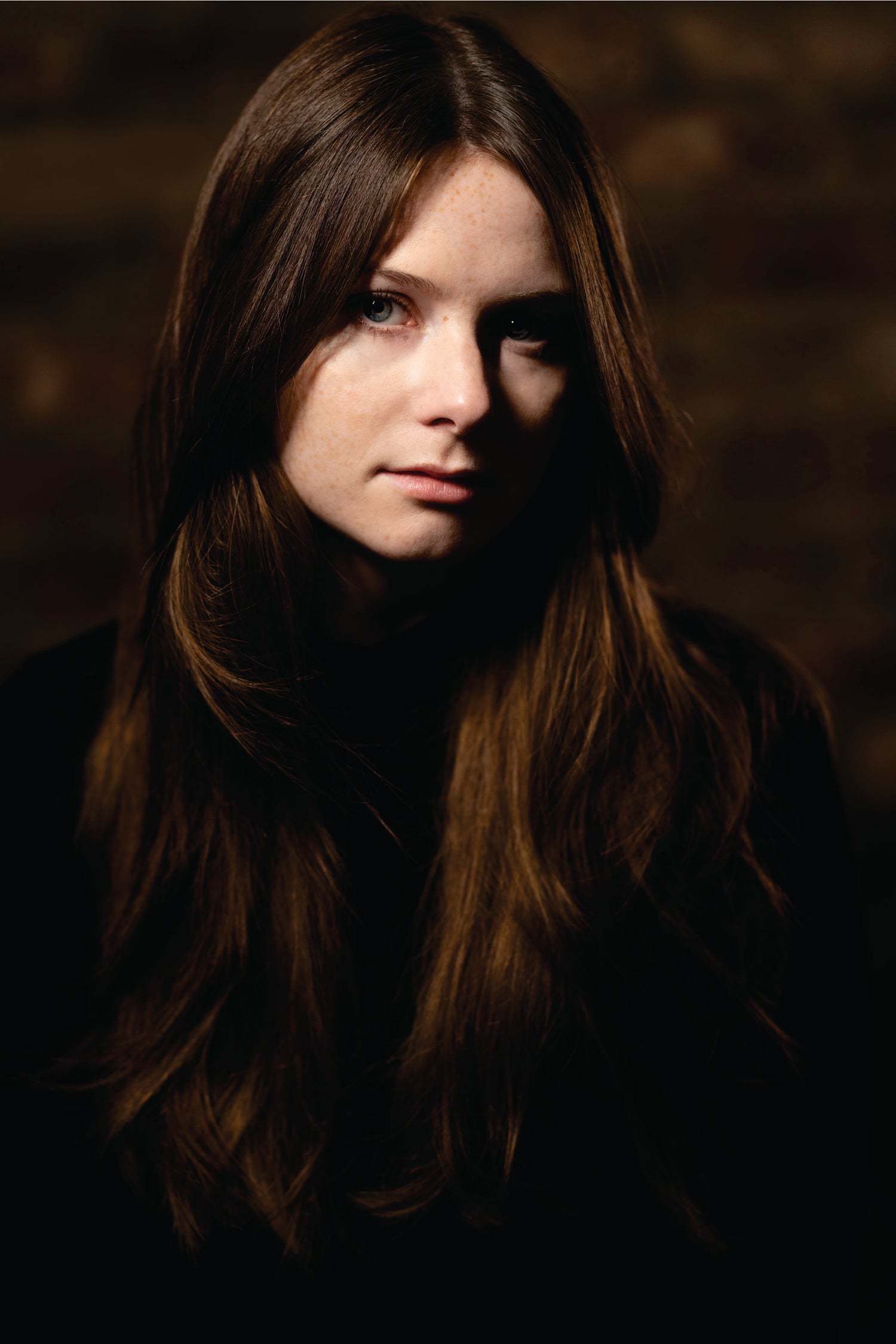 Dark portrait of a person with long hair against a blurred background