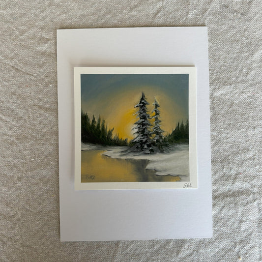 Small print of a snowy landscape with trees in a white frame on a textured surface.